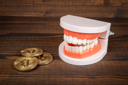 Bitcoin coin and teeth, wooden background. Concept of checking if valid, also dental costs concept