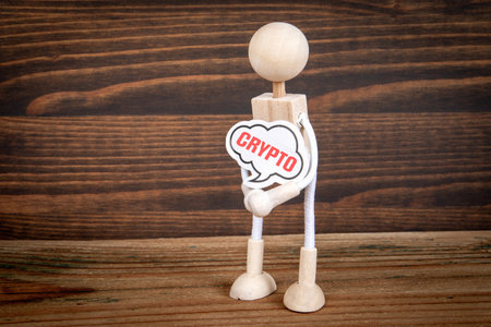 CRYPTO Concept. Miniature man with speech bubble in hands on wood texture background