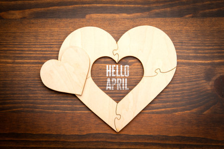 Hello April. Wooden puzzle in the shape of a heart on a wooden texture background