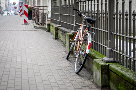 Abandoned Bicycle Leaning Against Fence on Paved Sidewalkの写真素材
