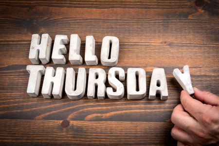 Hello Thursday. Concrete alphabet letters and coffee mug on dark wooden texture backgroundの写真素材