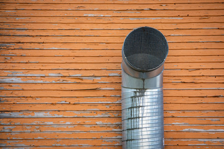 Industrial Ventilation Pipe on Weathered Wooden Wall with Peeling Orange Paintの写真素材