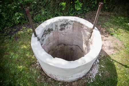 Open Concrete Water Well on Grass Yard Under Sunlight with Iron Support Barsの写真素材