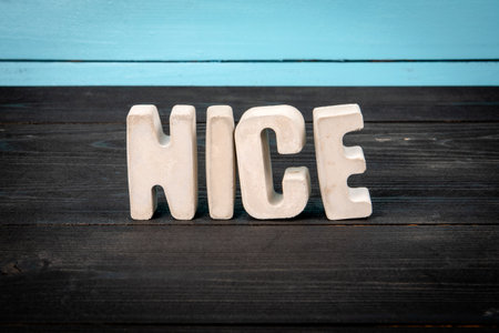 Word NICE in Concrete Letters on Wooden Surface with Blue Backgroundの写真素材