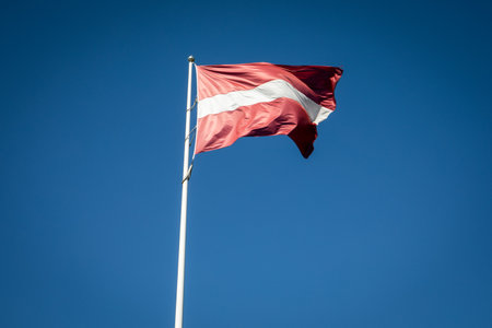 Latvian National Flag Fluttering in the Wind Against a Bright Blue Sky Backgroundの写真素材