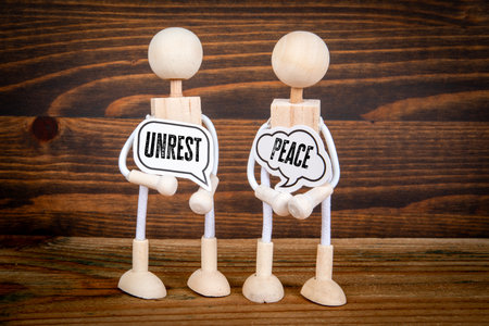 Contrast Between Peace and Unrest Represented by Wooden Figures Holding Speech Bubble Signs