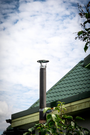 Modern Chimney Pipe on Green Metal Roof Against Cloudy Sky.