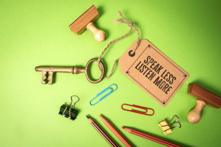 Golden Key With Tag Message Speak Less, Listen More on Green Background With Office Supplies