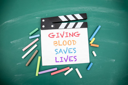 Giving Blood Saves Lives Message on Clapperboard with Chalk on Green Blackboard Backgroundの写真素材