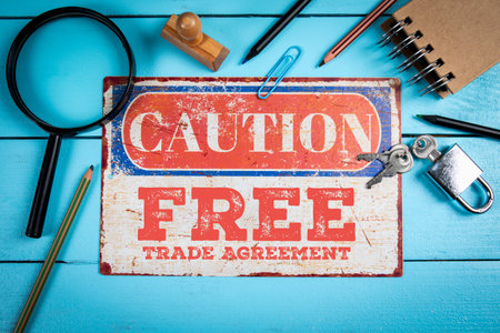 Caution sign about free trade agreement risks surrounded by business tools on blue deskの写真素材