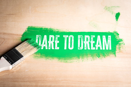 Paintbrush leaving a bold green stroke with the motivational phrase Dare to Dream on a wooden surfaceの写真素材