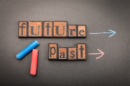 Concept of time with wooden letter blocks forming words Future and Past on blackboard, with arrows drawn in chalkの写真素材