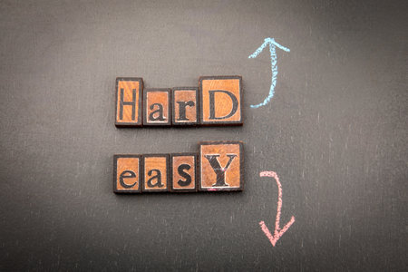 Wooden blocks spelling Hard and Easy with chalk arrows on dark background. Symbolizing difficulty, decision and life challengesの写真素材
