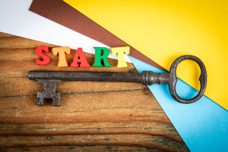 Colorful word START placed above an old key on wooden surface with bright paper backgroundの写真素材
