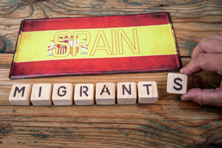 Spanish flag with wooden blocks spelling MIGRANTS. Symbolizing migration, society and national challengesの写真素材