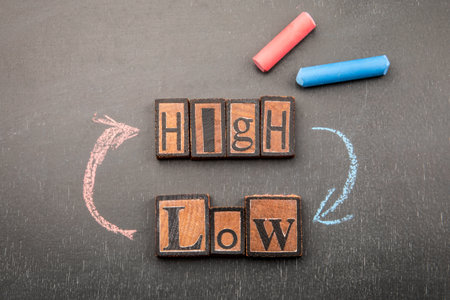 Conceptual image with wooden letter blocks spelling high and low, surrounded by red and blue chalk arrows on a dark backgroundの写真素材