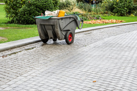 Garden maintenance cart with tools on wet cobblestone path in public park