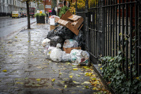 Stack of garbage bags and cardboard boxes on a rainy urban street. Waste management, pollution, and environmental issuesの写真素材