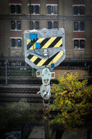 Metal crane hook featuring black and yellow warning stripes, symbolizing heavy industry, construction and workplace safetyの写真素材