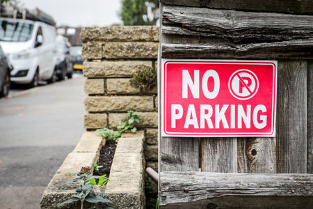 Red no parking sign on wooden fence near street and parked cars in urban areaの写真素材