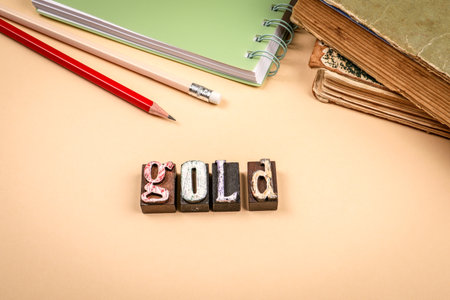 Word gold made from vintage wooden letterpress blocks with pencils and old books on beige backgroundの写真素材