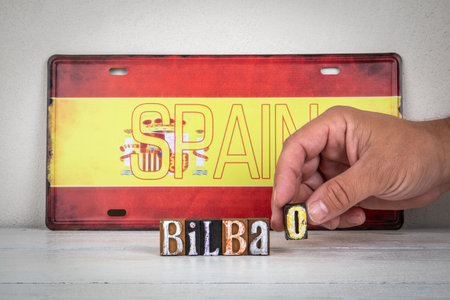 Word Bilbao made from vintage wooden letterpress blocks with hand arranging letters in front of Spain flagの写真素材