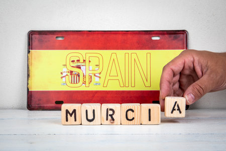 Hand placing wooden letter A to form the word Murcia in front of Spain flag license plate, travel and tourism conceptの写真素材
