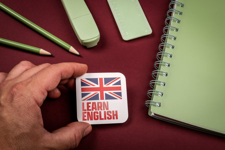 Hand holding Learn English card with United Kingdom flag surrounded by stationery items and notebookの写真素材