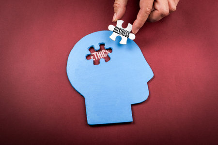 Hand placing Business puzzle piece into blue human head shape with word Ethics insideの写真素材