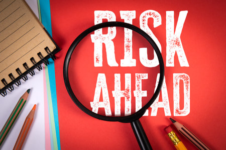 Magnifying Glass Highlighting Text Risk Ahead on Red Background Representing Danger and Caution Conceptの写真素材