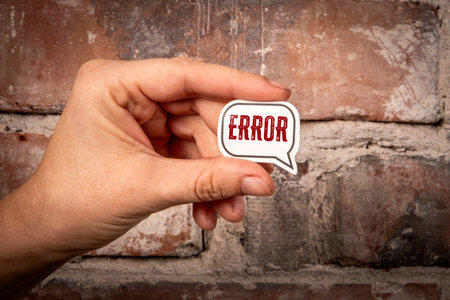 Hand Holding Speech Bubble with Word Error Against Brick Wall Representing Mistake and Problem...
