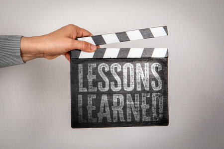 Lessons Learned Concept with Hand Holding Clapperboard on Gray Backgroundの写真素材