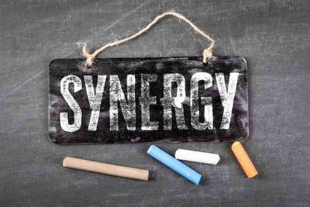 Synergy Business Concept With Hanging Blackboard Sign And Color Chalk On Deskの写真素材