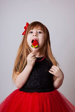 a girl in a smart black and red dress with a lollipop white backgroundの写真素材