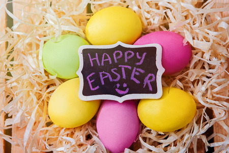 Easter eggs lie in the nest, the inscription on the chalk tablet Happy Easter