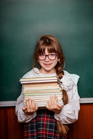 girl, schoolgirl in school uniform with a stack of books, against the background of a school boardの写真素材
