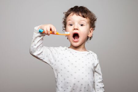 a little boy, a kid with a toothbrush in his hands and his mouth wide open, getting ready to brush his teeth. surprised. Enthusiastic look. Hygienic procedures. isolated white backgroundの写真素材