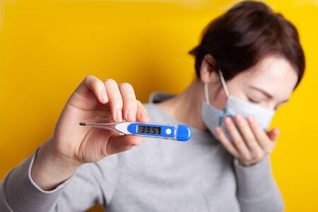 woman in medical mask coughing with fever. Holds a thermometer in his hands. Severe condition of a...
