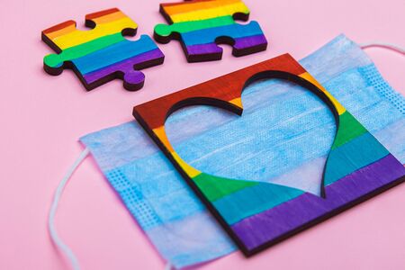 LGBT symbol puzzles and heart frame painted by a rainbow on a medical mask. Coronavirus quarantine, online festival and pride day 2020. copy-space. space for text on a pink background.の写真素材