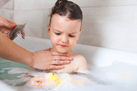 unhappy gay baby bathes in the bath with water and soap foam. Hygiene procedures every day.