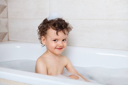 cute curly baby bathes in the bath with an emotional laugh. Personal hygiene rules for children....