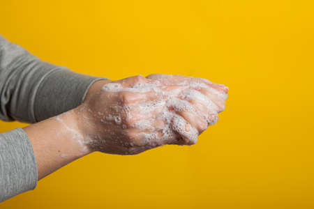 Instruction to carefully wash your hands and nails on a yellow background. Womens hands in a soap solution on a bright backgroundの写真素材