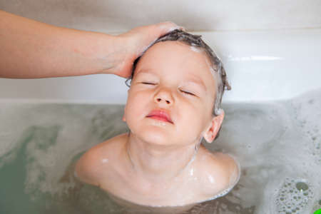 A small child washes his head throwing back and squinting his eyes so that the foam does not get...