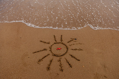symbol of the sun and a plane by the sea. Painted sun on the sand, sea coast, figure of a red plane, sea wavesの写真素材