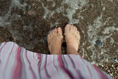 womens feet relax on the sand in sea water. A woman in a striped pink dress, a trip and a lifestyle on the coast of the seaの写真素材