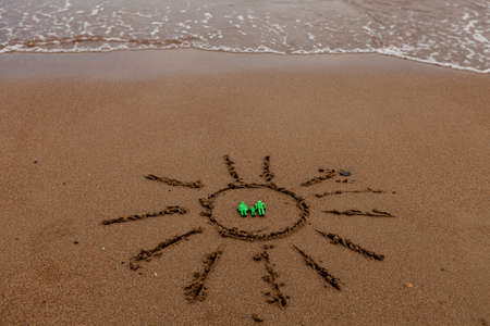memes. vacation by the sea. Recreation and tourism on the sea coast. The symbol of the family and the sun is painted on the sand near the waves of the seaの写真素材