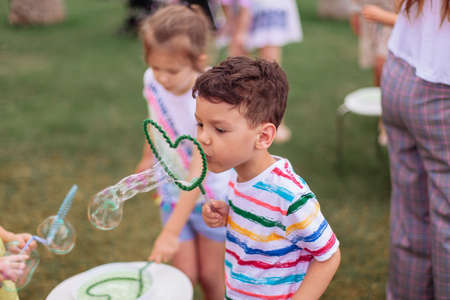 the child inflates large soap bubbles. Street animation program, happy child on a green lawn. Summer...