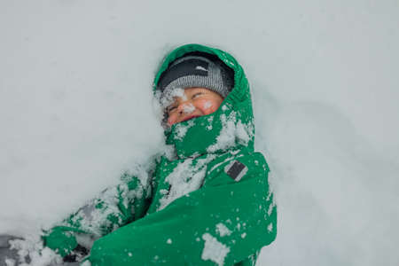 portrait of a happy child playing in the snow. There is snow on my face. The boy plays snowballs, a snow-stained face, winter dynamic games.の写真素材