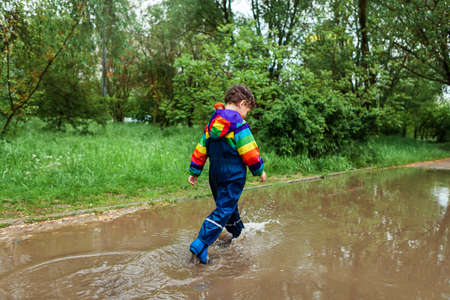 the boy runs and jumps through puddles in a waterproof suit and rubber boots.Bright kurta in the...