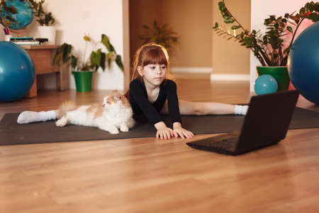 the girl sits on twine at her laptop. Online training in sports and stretching.